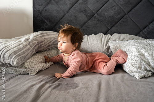 Small caucasian baby lying down on the belly on the bed with wet urine stain on the sheet and clothes looking to the side Bedwetting child pee on the bed