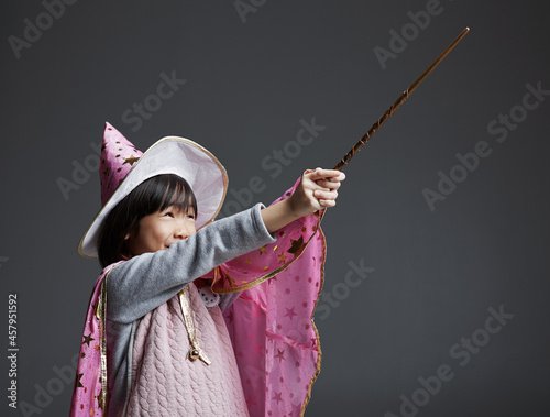 Cute Asian little girl wearing magic dress , playing with magic wand indoors