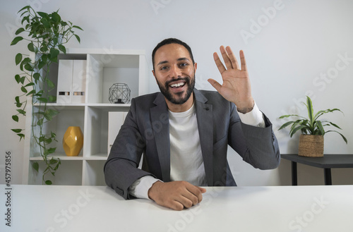 African american man in video call waves hand saying hello to coworker. Latino CEO looking at camera in business meeting