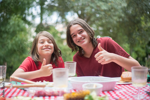 Happy children eating together. Two schoolboys enjoying food. Showing thumbs up. Family time, outdoor activity, picnic concept