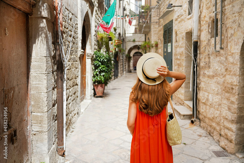 Back view of female tourist walking in narrow alley of medieval old town of Bisceglie, Apulia, Italy