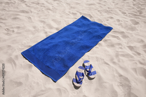 Flip flops and blue beach towel on sand