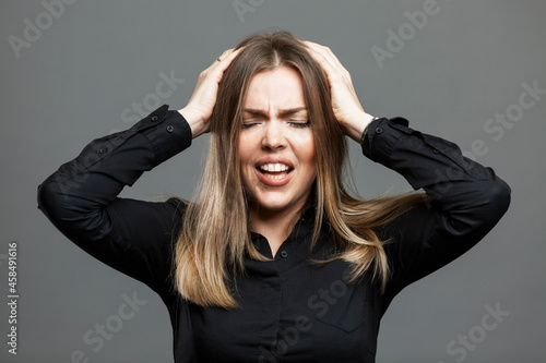 A young woman holds her head with her hands. Pain and negativity. Gormanalnye change and PMS. Beautiful blonde in a black shirt. Gray background.