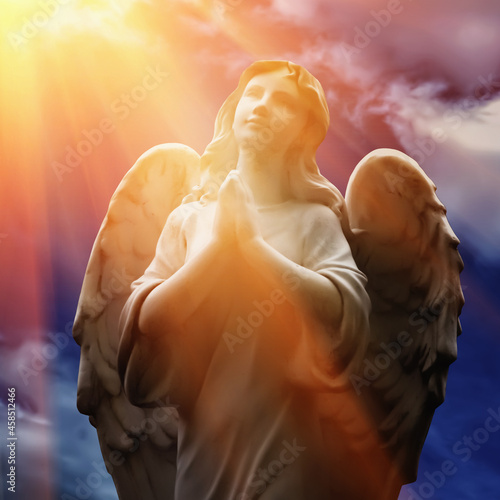 Beautiful angel with wings looking up at the sky in rays of light. Ancient statue.