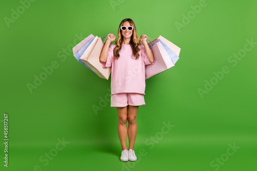 Photo of impressed pretty young lady wear pink shirt dark glasses rising bargains smiling isolated green color background