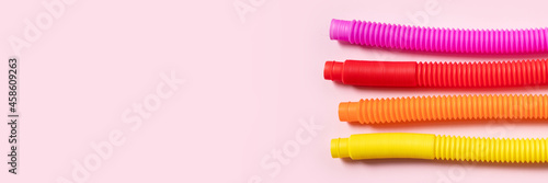 Colorful anti-stress fidget push pop tube sensory toys for children on pink background. Top view, flat lay. Close-up of creative game with popular plastic flexible bright corrugated pipe. Banner