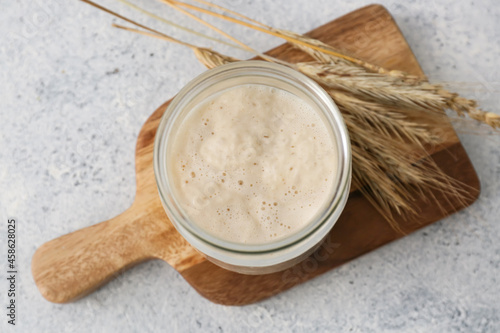 Jar with fresh sourdough and spikelets on white background