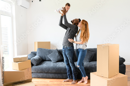 Happy mixed-race family relocated in new house, African-American husband and caucasian wife standing with a cute biracial daughter surrounded cardboard boxes