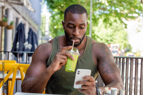 Mid adult man drinking smoothie and using smart phone