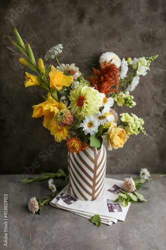 A flower arrangement of dahlia and zinnias in a high vase against a dark background. Floristics. Home decoration.