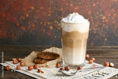 Glass of tasty latte with nuts and cookies on table