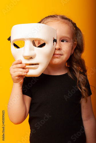 a cute little girl holds a theatrical mask on the floor of her face for the day of the theater, the day of the actor. Depicts mimes