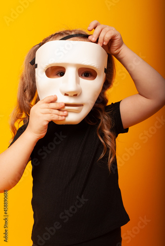 cute little girl child holds a theatrical mask by the face playing a role on the day of the theater, the day of the mime. little actress