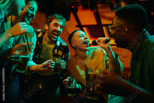 Cheerful friends having fun while singing karaoke during their night out in a pub.