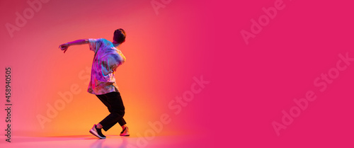 Back view of young stylish man dancing hip-hop isolated over colorful gradient background in neon light. Flyer