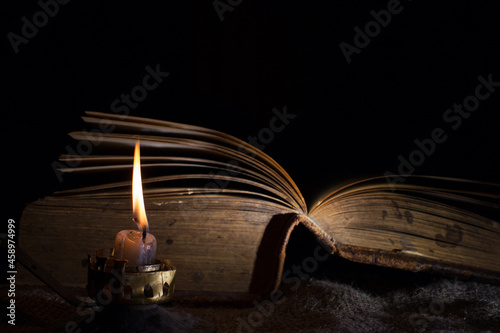 A candle burns next to an open old book. the concept of secret knowledge and mysticism. Selective focus on a candle flame.