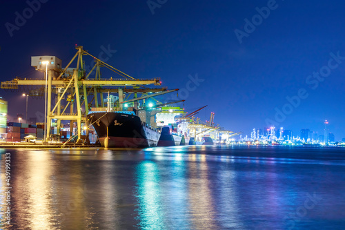 Container cargo ship with ports crane bridge in harbor and refinery industrial at night logistics and transportation concept