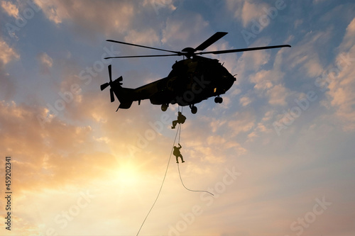 silhouette of military commando helicopter drops between are in flight for operation battle combat in sunset