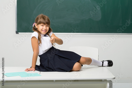 Happy school girl sitting on desk in classroom