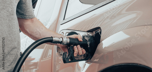 Closeup of man hand holds black gas pump nozzle pouring gasoline into the fuel tank of a vehicle at self service petrol station. Grey truck at gas station refueling petroleum by a car driver.