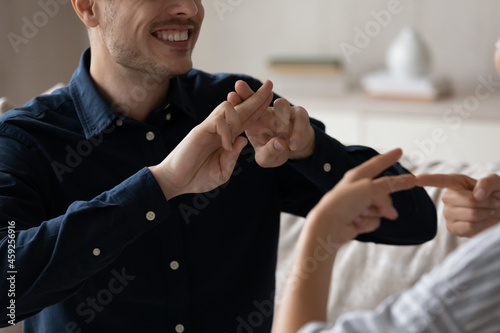 Close up cropped image smiling young deaf dumb family couple using sign language for communication. Happy millennial man and woman with hearing disability showing gestures, expressing feelings.