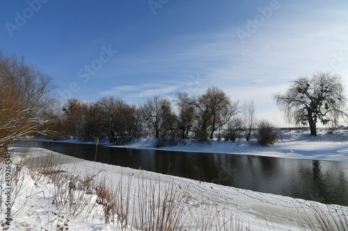 Winter landscape with snow-covered trees and river on a sunny day