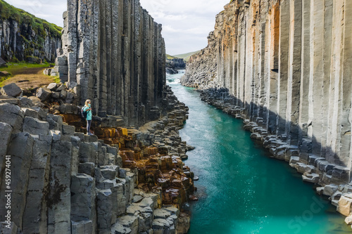 Woman hiker with backpack enjoying Studlagil Canyon. Unique Jokulsa basalt colums and A Bru river. Spectacular outdoor scene of Iceland, Europe. Beauty of nature concept background