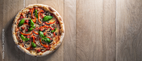 Pepperoni pizza with hunters sausages, mushrooms, red peppers and fresh basil on a wooden table