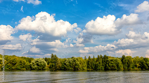 River landscape with trees on the shore and a blue cloudy sky