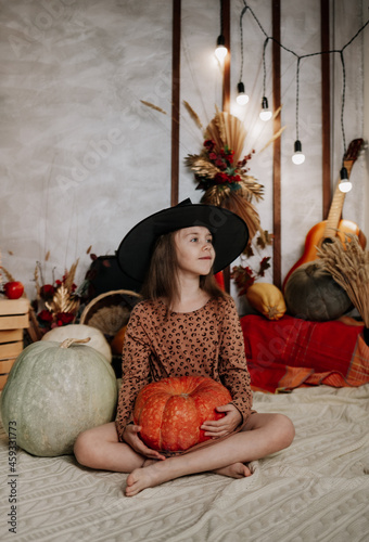 a little girl in a witch's hat is sitting on a knitted blanket with pumpkins