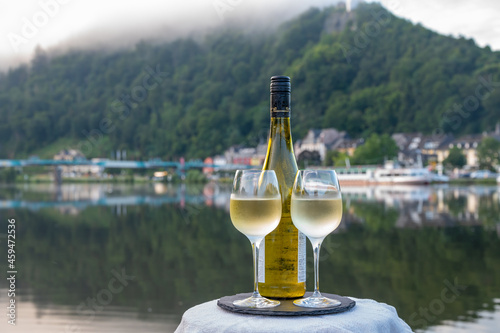 Tasting of white quality riesling wine served on outdoor terrace in Mosel wine region with Mosel river and old German town on background, Germany