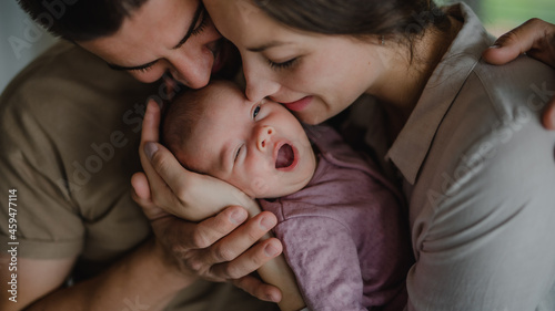 Close up of young parents holding and kissing their newborn baby indoors at home