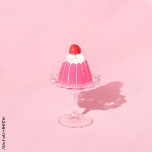 Pink jello on dish with cherry on top on pastel pink background. 70s or 80s retro style aesthetic dessert idea. Minimal food concept.