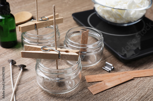 Glass jars with wicks and clothespins as stabilizers on wooden table. Making homemade candles