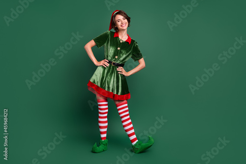 Photo of funny positive cheerful helper lady hands hips wear elf costume hat stockings isolated green color background