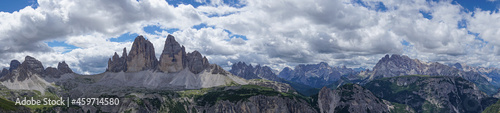 Three peaks in the Italian dolomites. Mountain panorama with clouds and blue sky. High alpine landscape with grass and stones. Wide panorama picture. Landscape photography