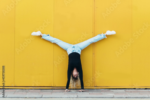 Woman doing hand stand while in front of the yellow wall