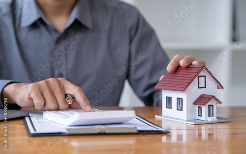 Businessman's hand calculating invoice with house model in office, man calculating house tax financial for buying a new home budget