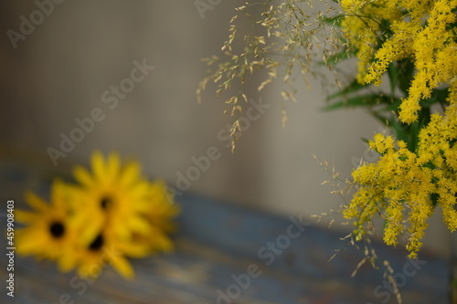 Solidago and poa grass bouquet on bokeh vintage, background with blurr rudbeckia flowers, floral, botanic background with space for text, autumn image with yellow flowers.