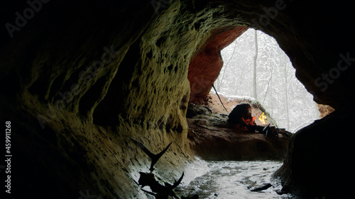 Wild caveman sitting near bonfire in dark cave