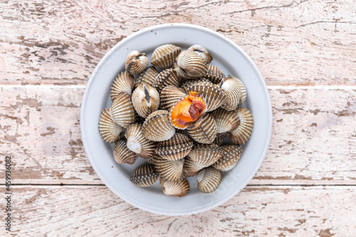 fresh steamed cockles, boiled cockles in ceramic plate on old white wood texture background, top view, light and airy food photography, blood cockle