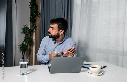 Young businessman sitting in an office and shields or hide a laptop screen with his hand because a colleague sent him inappropriate adult content in an email as a joke while he working