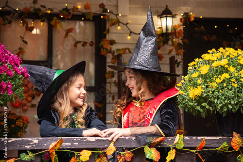 Happy Halloween! Two cute little laughing girls in witches costumes are coming to the house for sweets.
