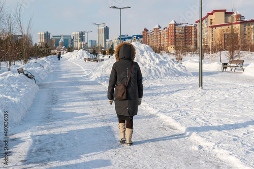 A woman walks along a snow-covered street in city of Krasnoyarsk. View from back. Concept of winter season in Siberia.