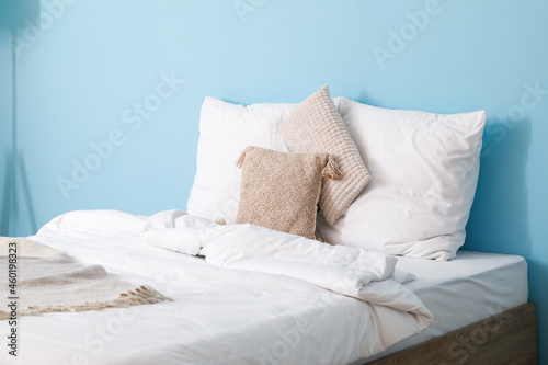Comfortable bed with soft pillows and blanket near blue wall