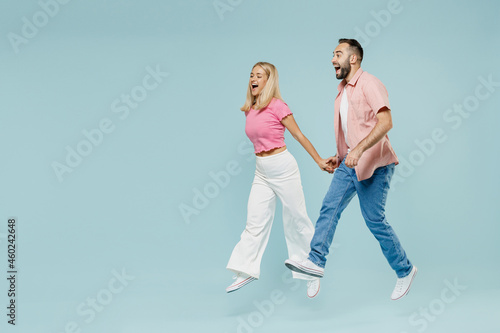 Full body young couple two friends family man woman in casual clothes jump high hurrying up go walk together isolated on pastel plain light blue background studio portrait People lifestyle concept