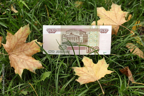 100 rubles of 1997 design. Bank of Russia banknote of 1997 with a denomination of 100 rubles. banknote of 100 rubles on the grass. Dry leaves of the Canadian maple. Autumn