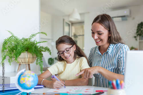 Cute girl with mother doing homework at home. A mother helps her little daughter to do her homework for the school. Education and family concept