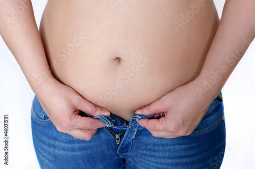 Woman with naked belly tries to fasten her jeans, overweight and diet. Weight loss concept, slimming and obesity