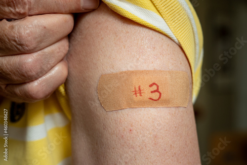 Senior caucasian man holding up shirt sleeve to show the bandaid after the booster coronavirus vaccine shot in the shoulder